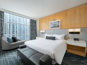 A modern hotel room with a large bed, a sofa, a bedside table, and a view of the cityscape.