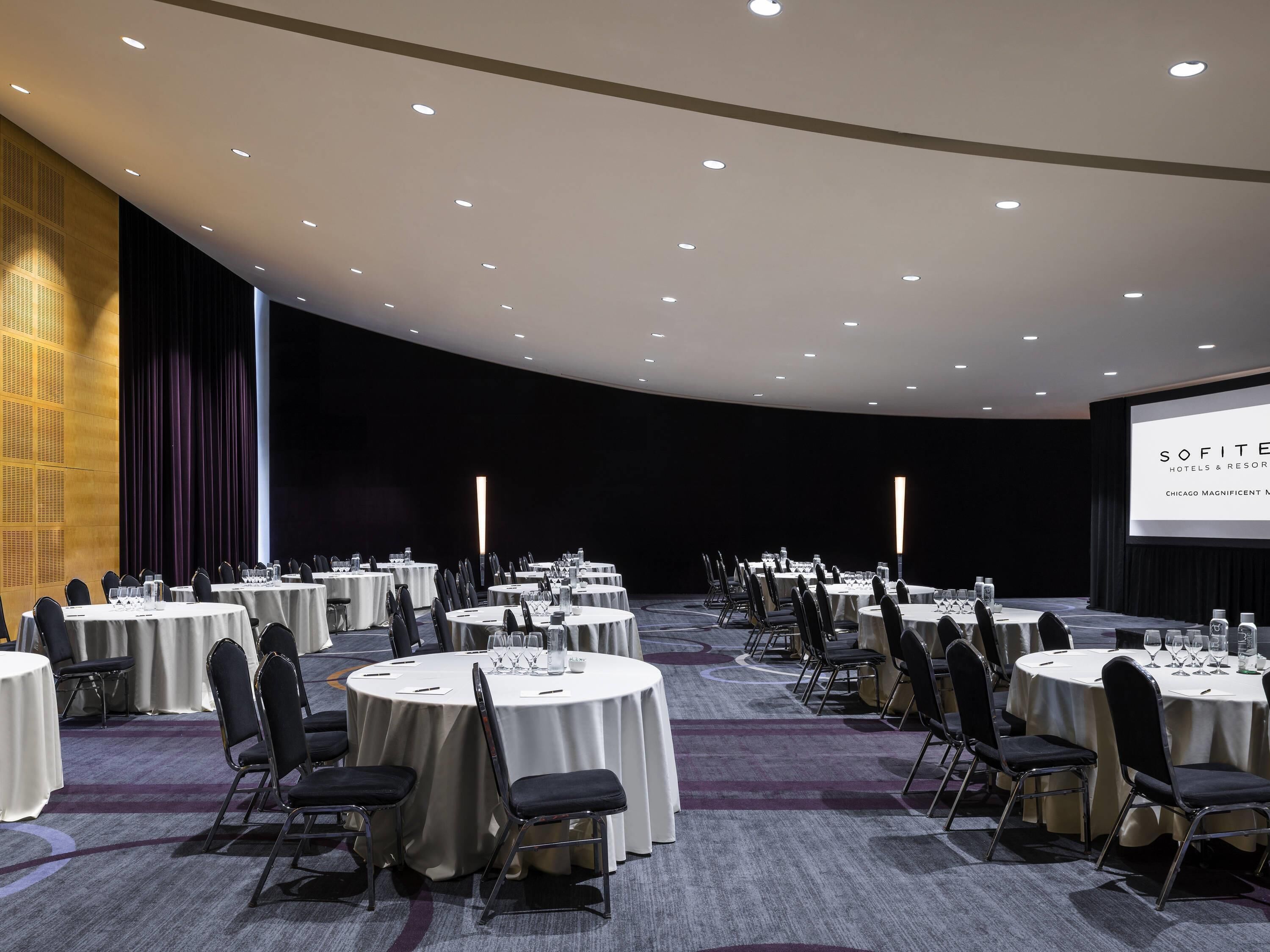 A conference room with round tables, chairs, and a projection screen.