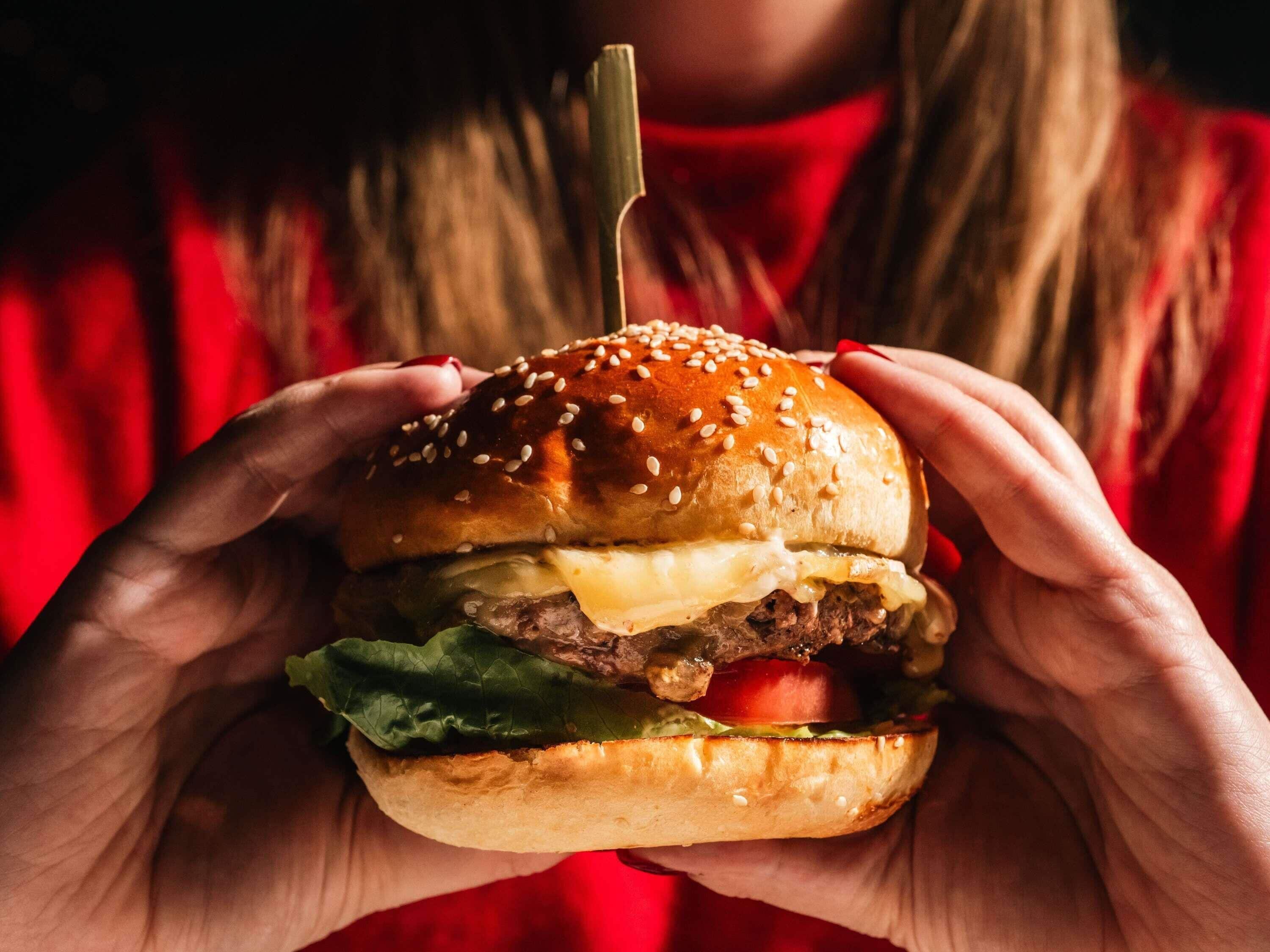 Una persona sosteniendo una hamburguesa con ingredientes visibles como lechuga, tomate y queso.