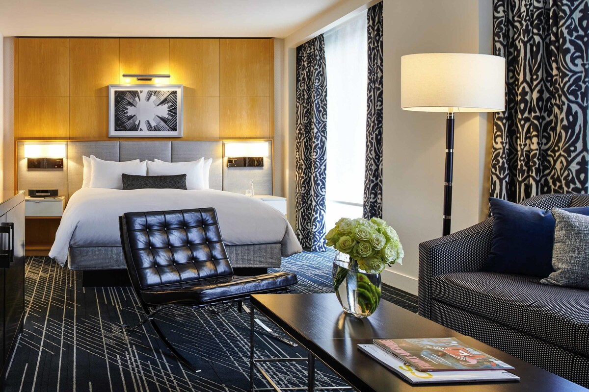 A hotel room with a bed, a sofa, a coffee table, a lamp, and a vase with flowers.
