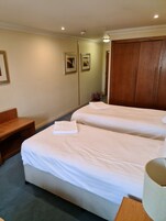 Una habitación de hotel con dos camas, una mesita de noche de madera, una pequeña mesa y un armario.