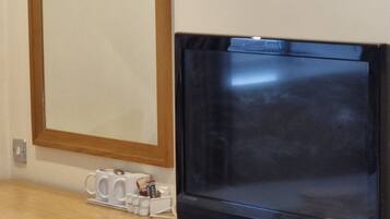 A wooden desk with a flat-screen TV, a mirror, and a few items on the counter.