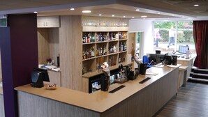 Zona de bar con mostrador de madera, estantes con botellas, una cafetera y un monitor de computadora.