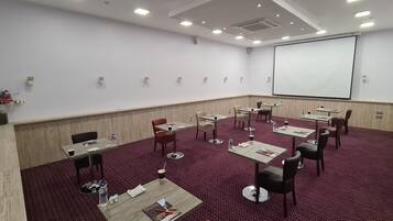 A conference room with a large screen, multiple tables with chairs, and a carpeted floor.
