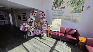 Un área de recepción con un arreglo floral, un sofá rojo y carteles informativos en la pared.