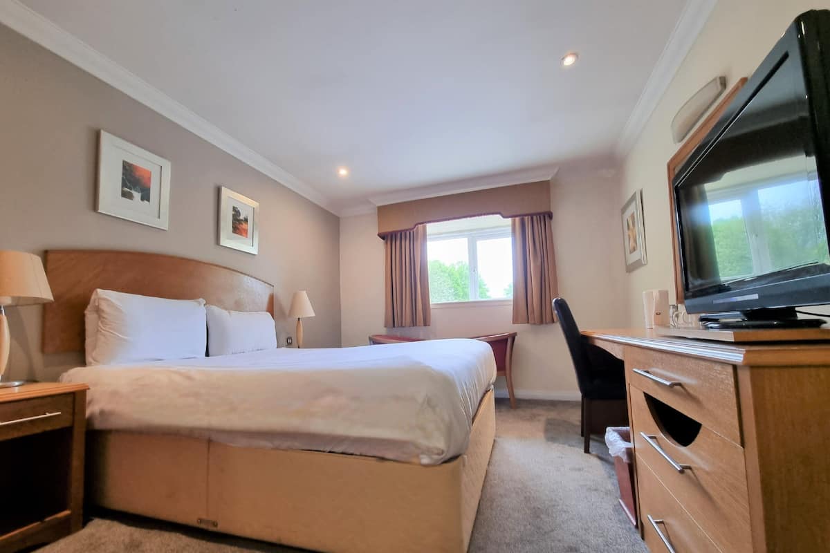 A hotel room with a large bed, a desk, a chair, a television, and a window with curtains.