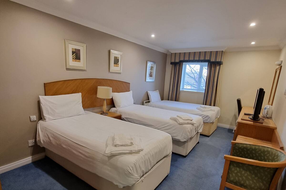 A hotel room with three beds, a desk, a chair, and a window with curtains.