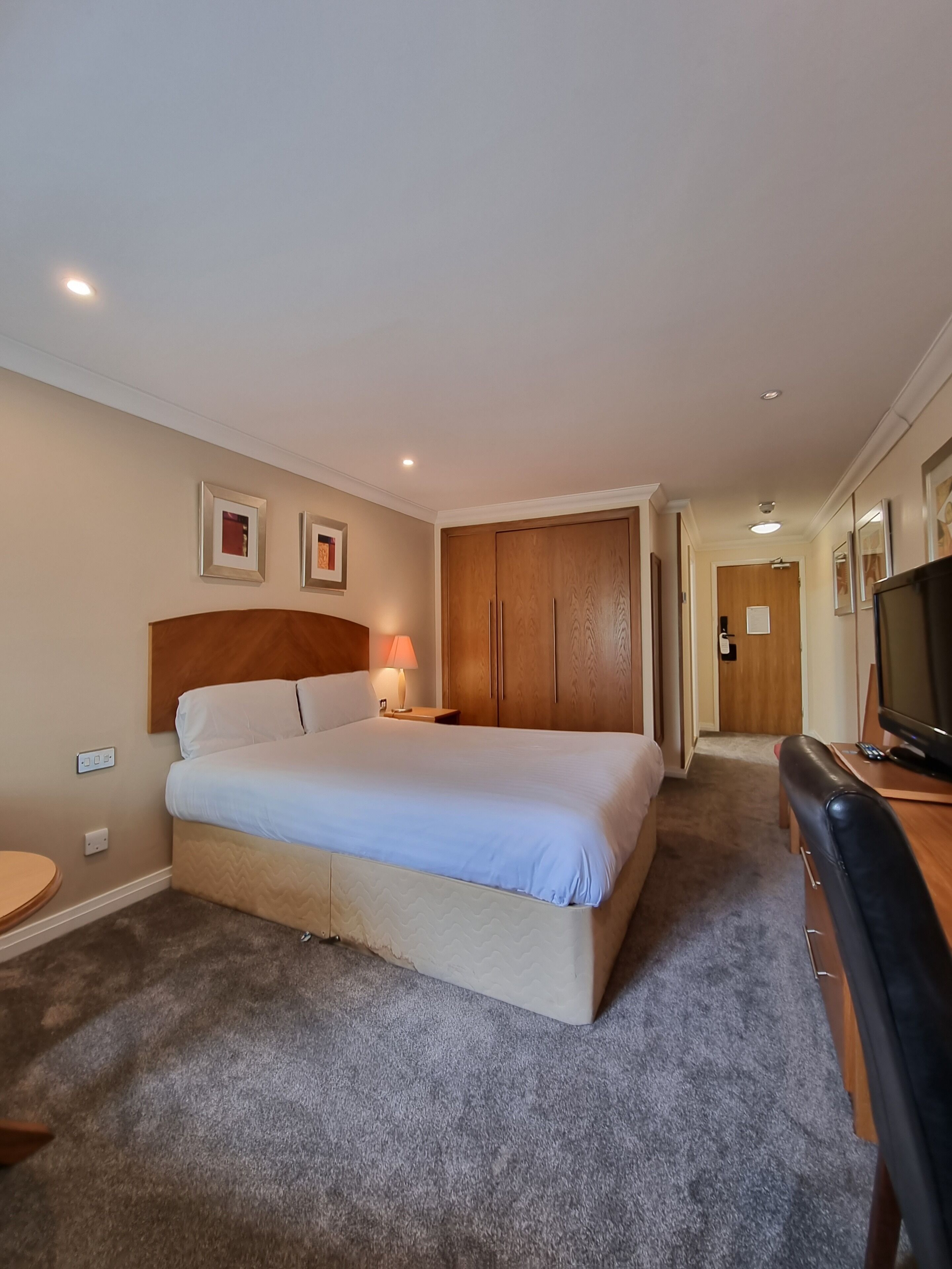 Una habitación de hotel con cama, escritorio, televisor y armario.