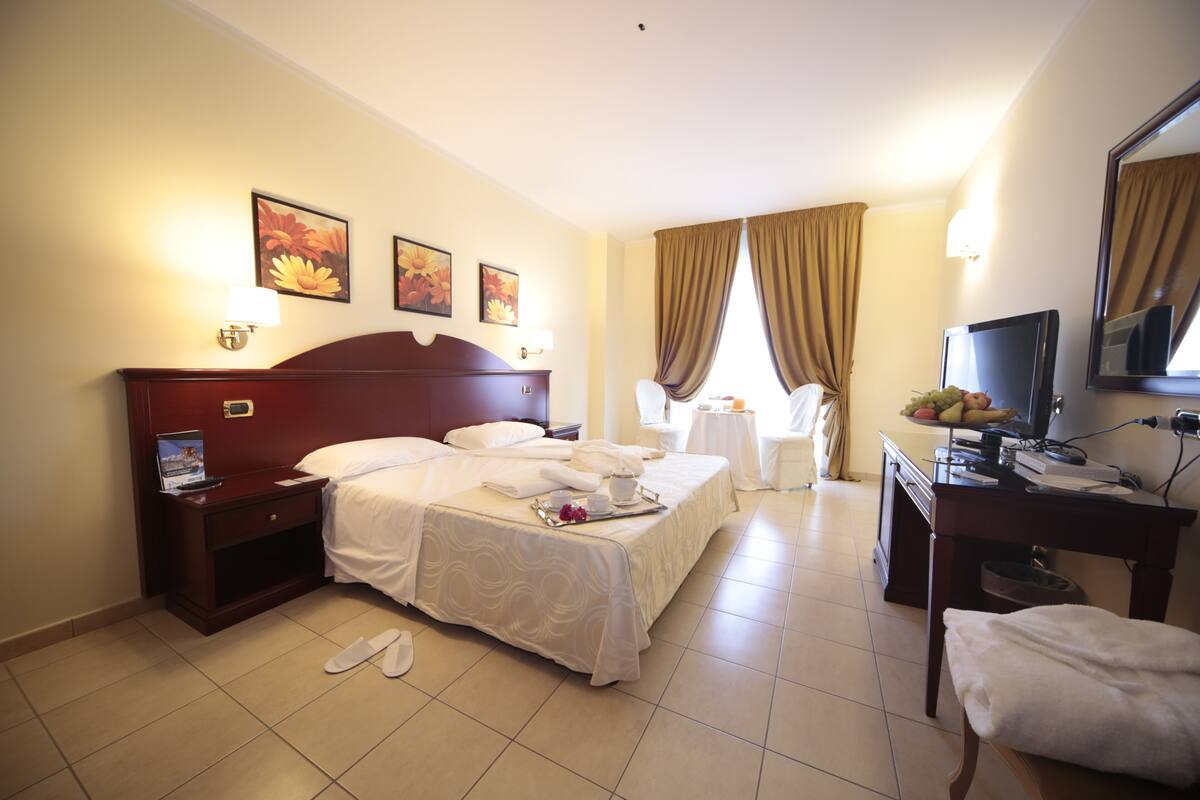 Una habitación de hotel con cama, mesita de noche, silla, escritorio y televisor.