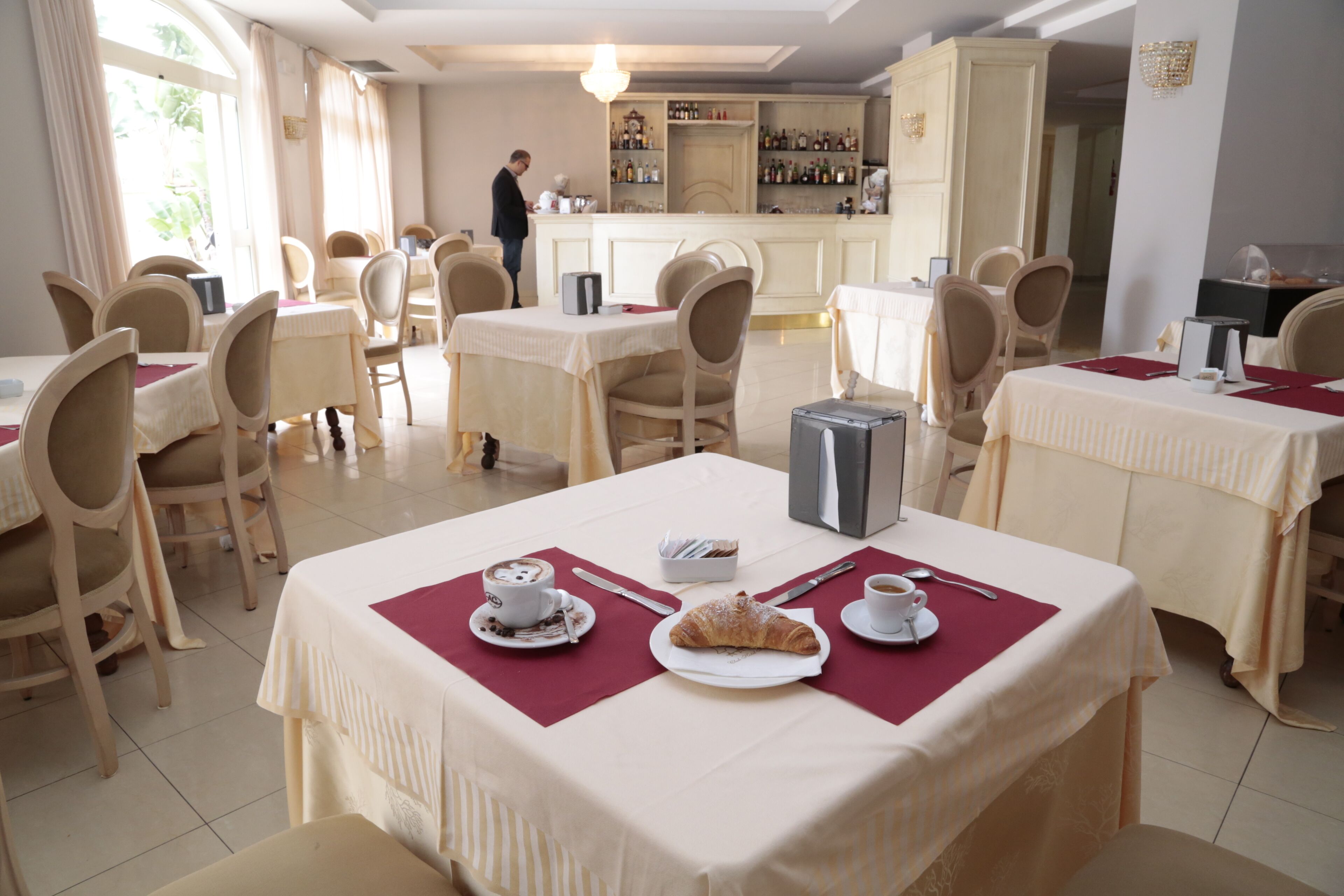 A dining area with tables set for breakfast, including croissants and coffee, and a bar area with bottles.