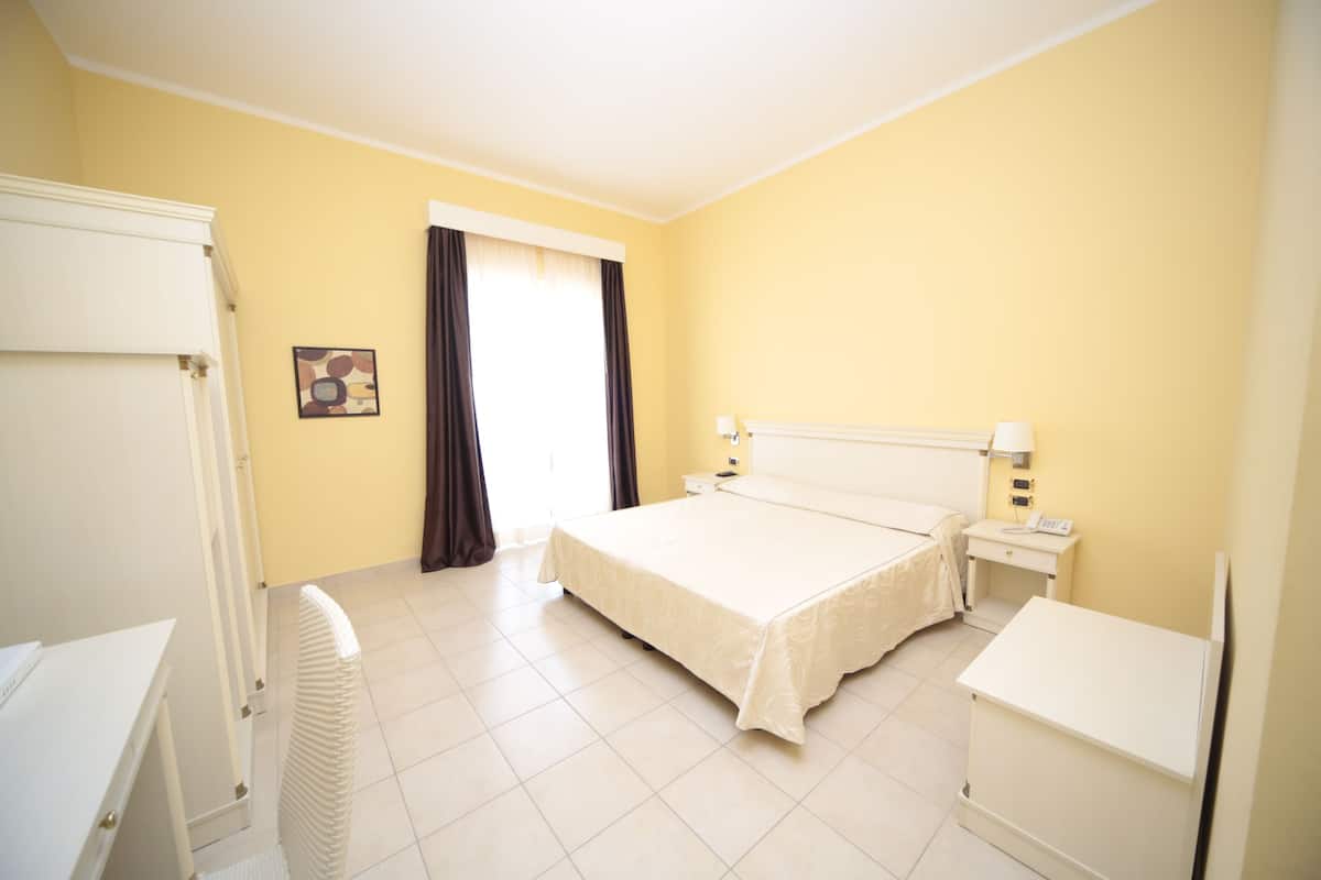 Una habitación de hotel con una cama, mesitas de noche, un escritorio y un radiador.