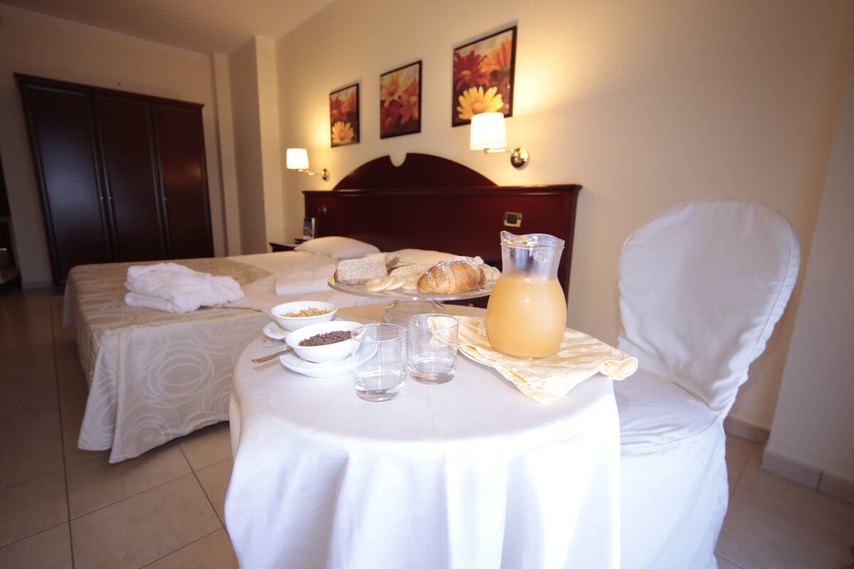 Una habitación de hotel con dos camas, una mesa de comedor con alimentos para el desayuno y una jarra de jugo.