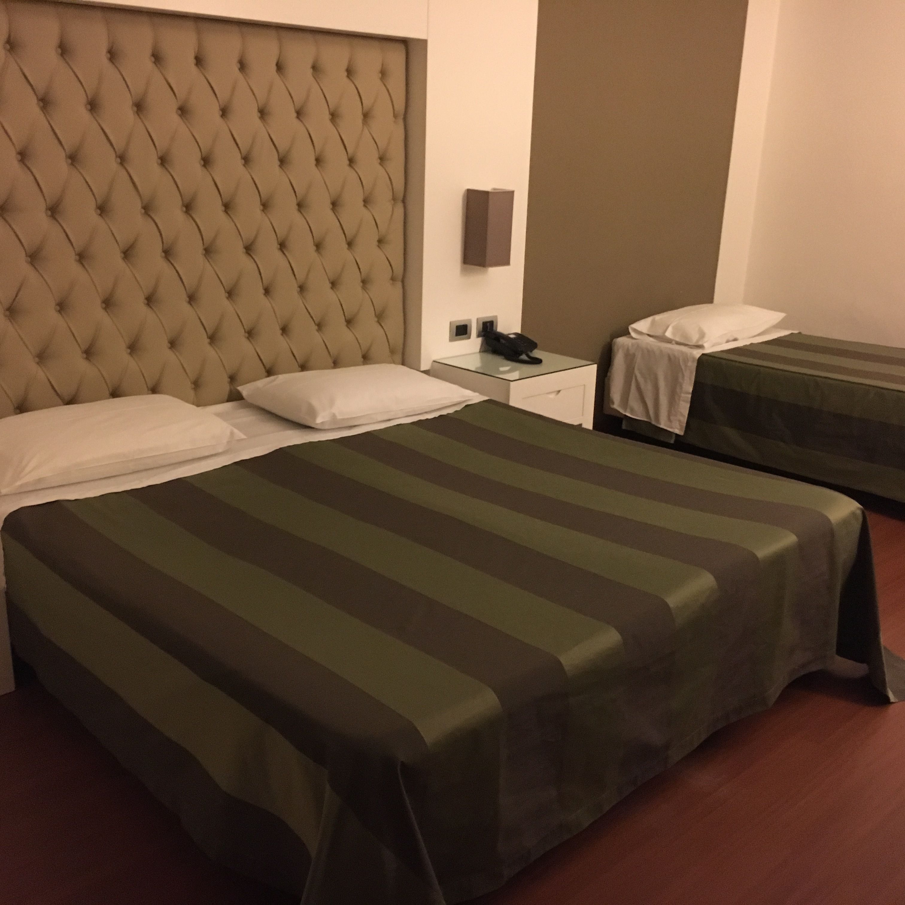 A hotel room with two beds, a tufted headboard, a bedside phone, and a nightstand.