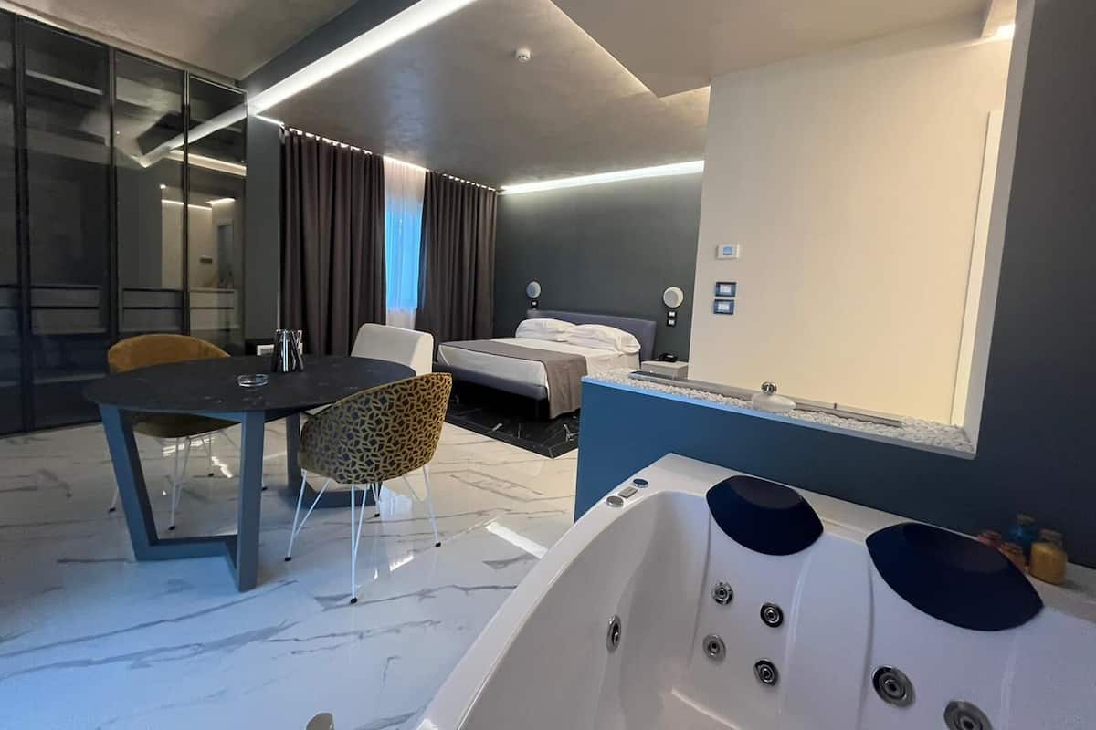 Una habitación de hotel moderna con una cama grande, un área de descanso con una mesa y sillas, una bañera y un espejo amplio.