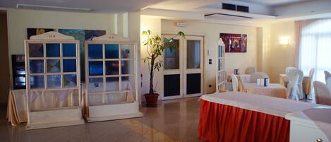 Habitación de hotel con cama, planta en maceta, zona de comedor con sillas y vista al exterior.