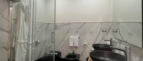 Un baño moderno con cabina de ducha de vidrio, un bidé negro, un tocador de madera con lavamanos negro y paredes de mármol.