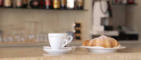 Une tasse de café et un croissant sur un comptoir en marbre, avec en arrière-plan, flou, des étagères remplies de bouteilles.