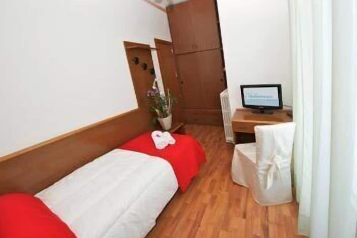 A small hotel room with two single beds, a desk with a computer, a chair, and a potted plant.