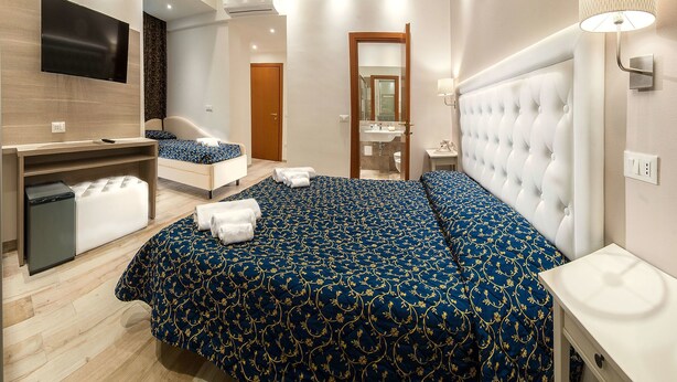 Una habitación de hotel moderna con una cama grande, un televisor montado en la pared, un escritorio con un ordenador y un refrigerador pequeño.