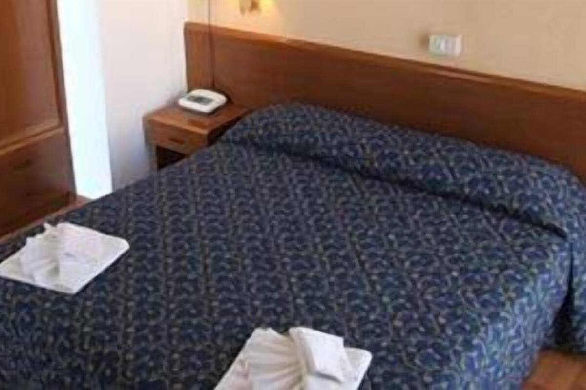 A bedroom with a bed, a wooden wardrobe, a nightstand with a scale, and a wall socket.