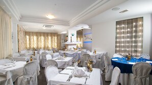 Un comedor formal con varias mesas dispuestas para el servicio, manteles blancos y sillas cubiertas de blanco.