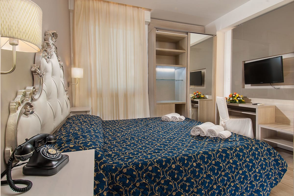 A hotel room with a bed, a desk, a telephone, a television, and a mirror.