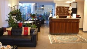 Un vestíbulo de hotel con una recepción, zona de estar y plantas en macetas.