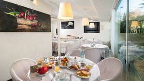 Un comedor con mesas redondas, sillas blancas y un cuadro con frutas en la pared.