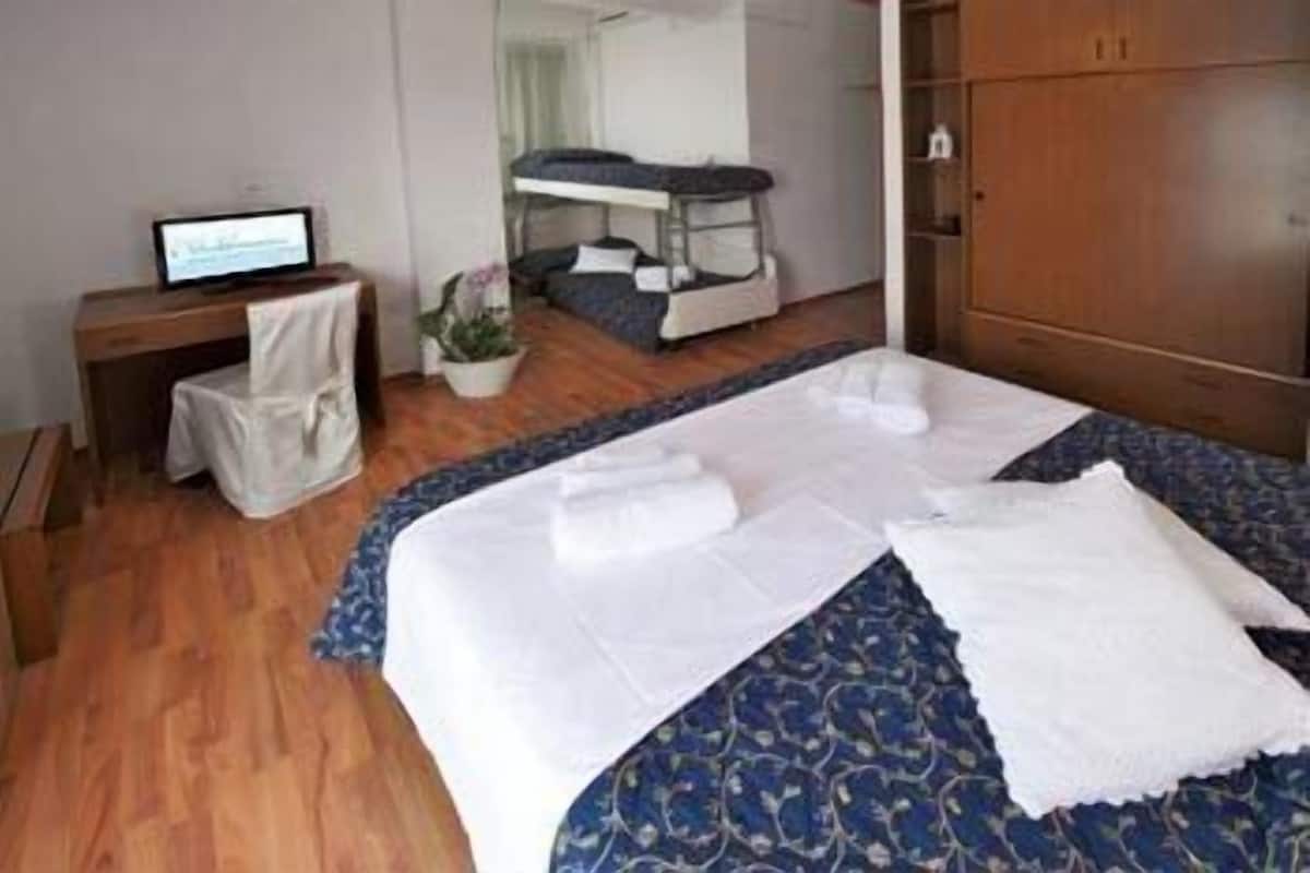 A hotel room with a bunk bed, a desk with a computer, a chair, and a wardrobe.