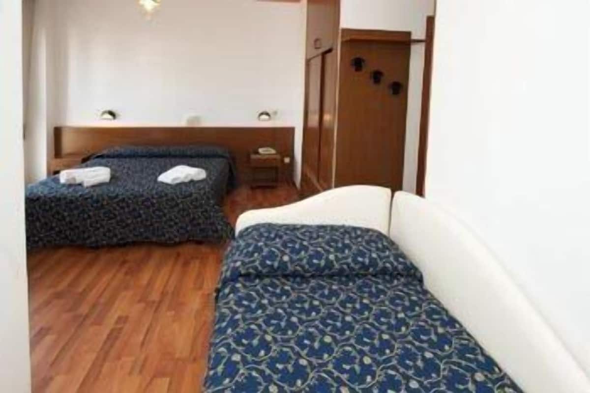 A small, compact room with two beds, a wooden wardrobe, and a small table.