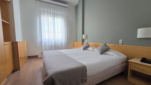 Ein Hotelzimmer mit einem großen Bett, einem Nachttisch mit Telefon, einer Lampe und einem Kleiderschrank.
