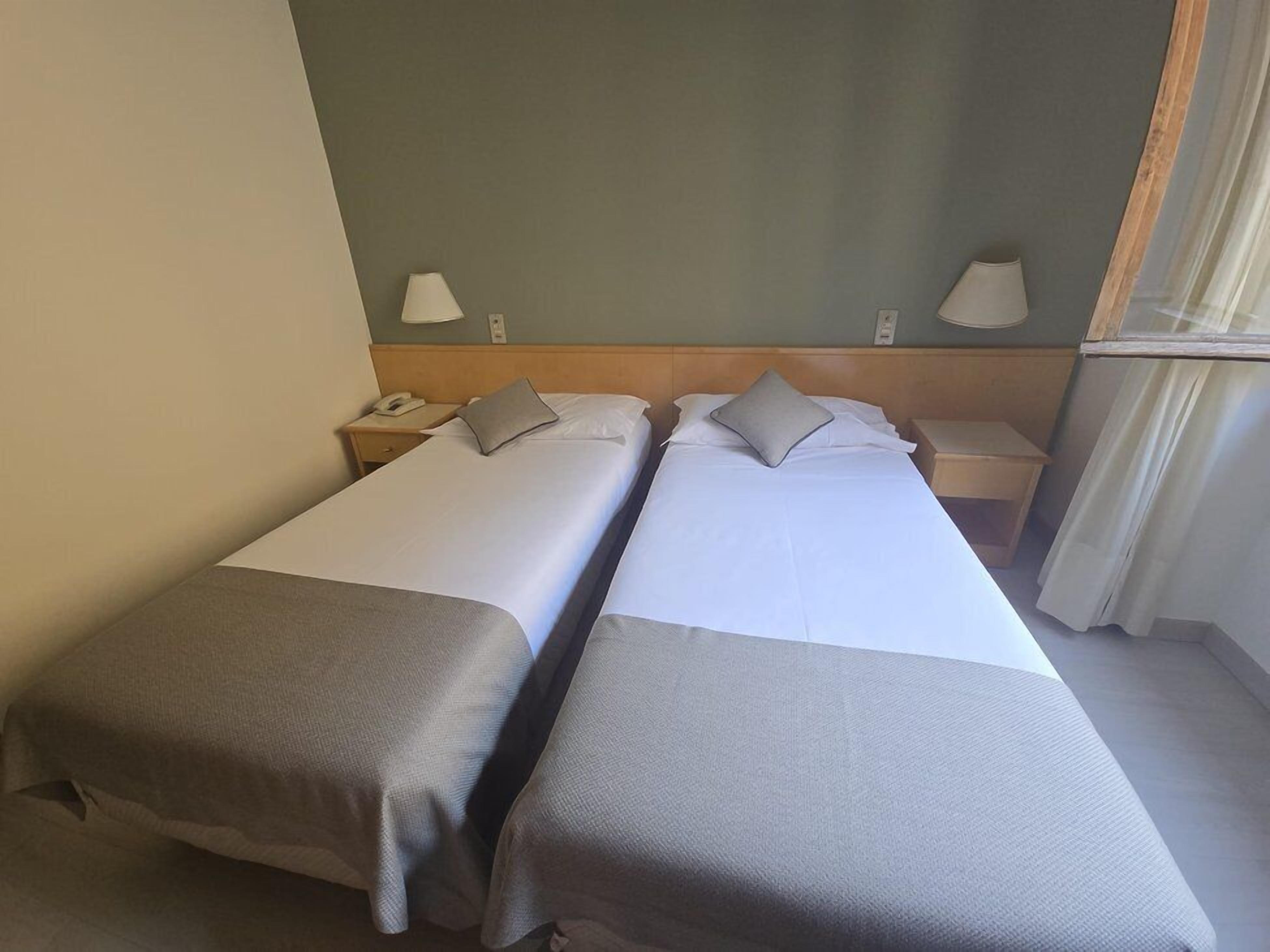 Une chambre d’hôtel avec deux lits simples, chacun étant équipé d’un oreiller et d’une table de chevet avec une lampe.