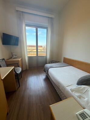 A hotel room with a bed, a desk, a chair, a TV, and a window with a view of buildings. - Mokinba Hotels Sant'Ambroeus (Milan)