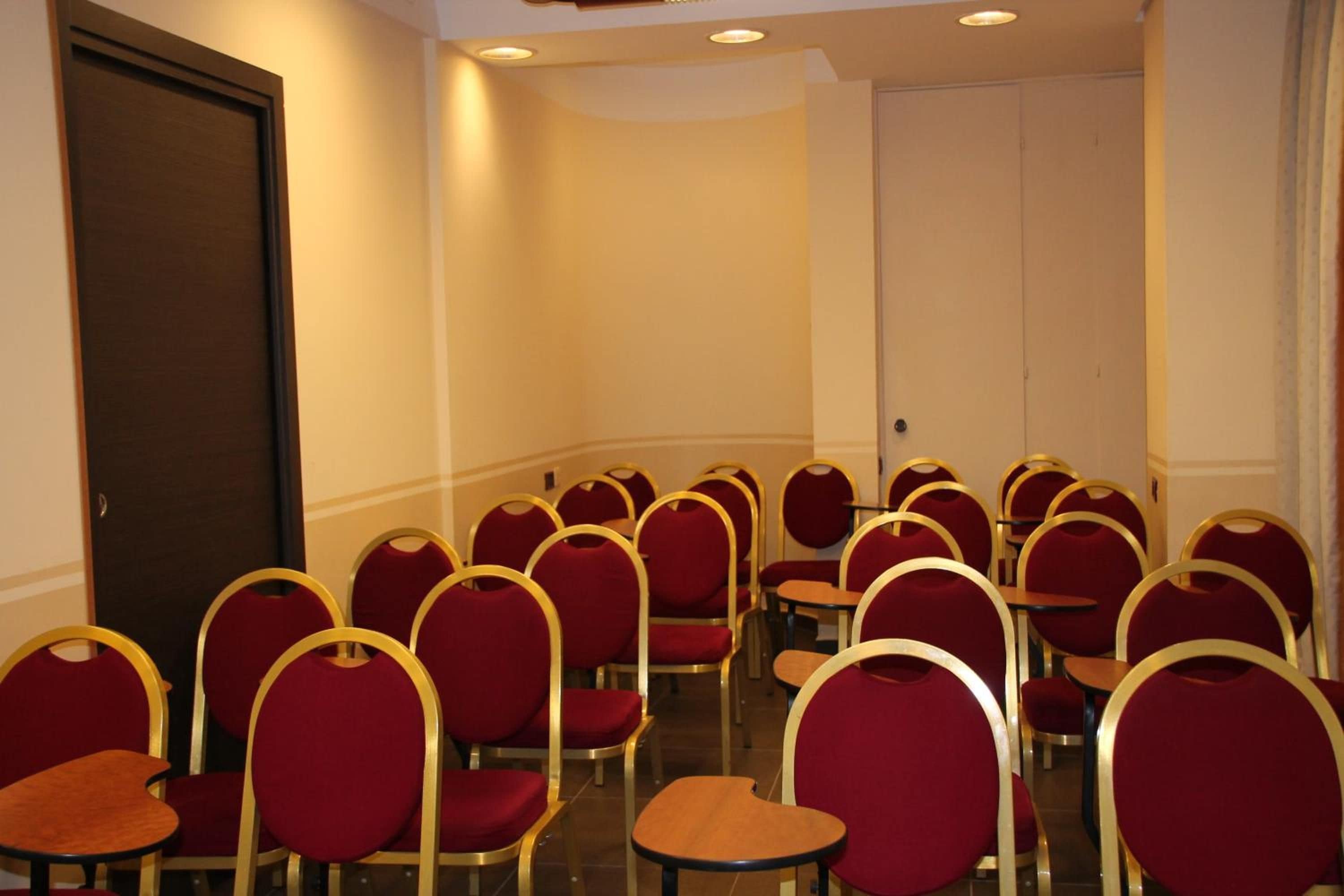 A conference room with rows of red chairs and tables, a door, and a white wall.