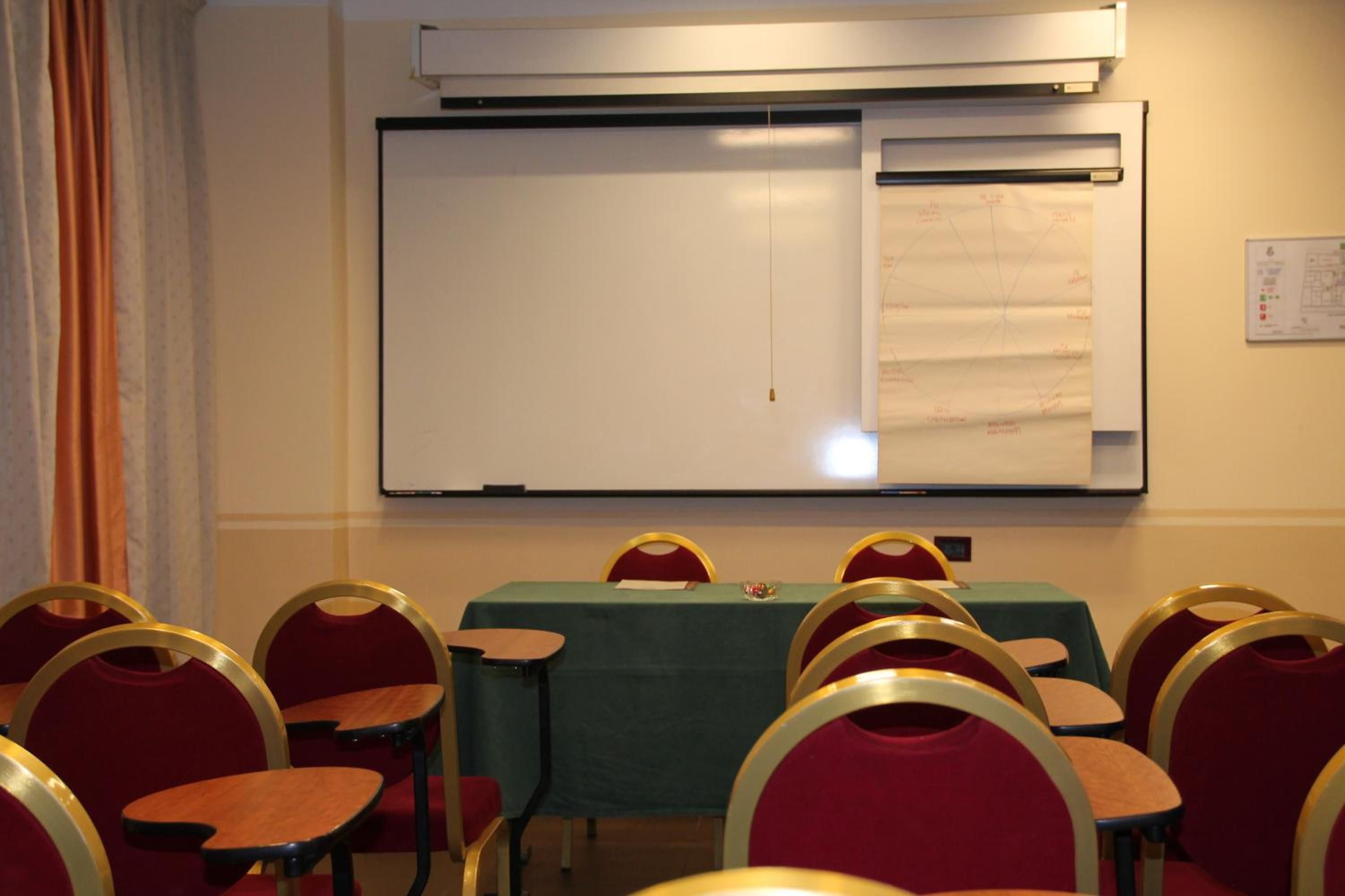 Un salón de conferencias con una pizarra, una mesa cubierta con mantel verde y sillas rojas con detalles dorados.