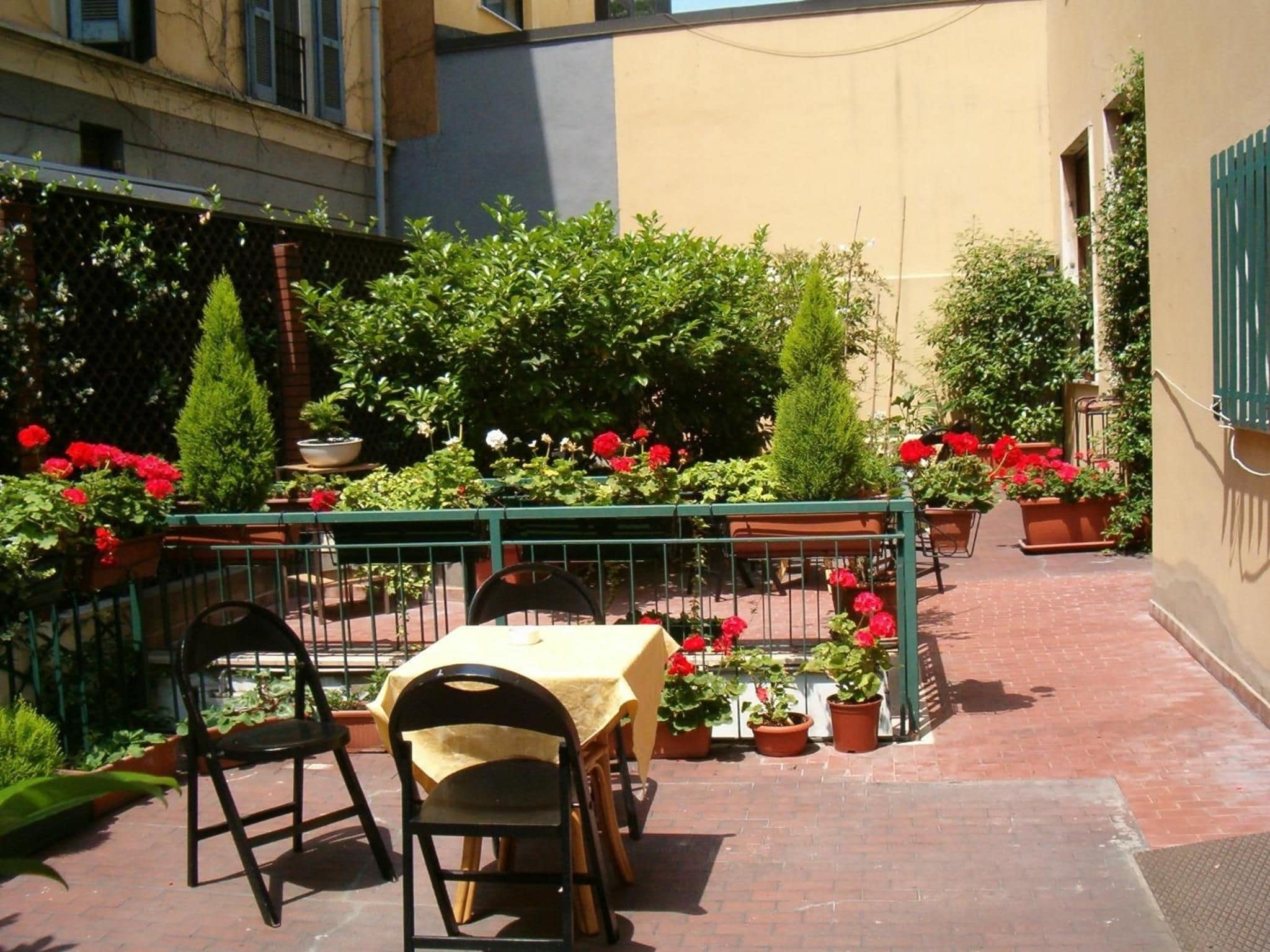 An outdoor patio with a table and chairs, surrounded by potted plants and flowers.