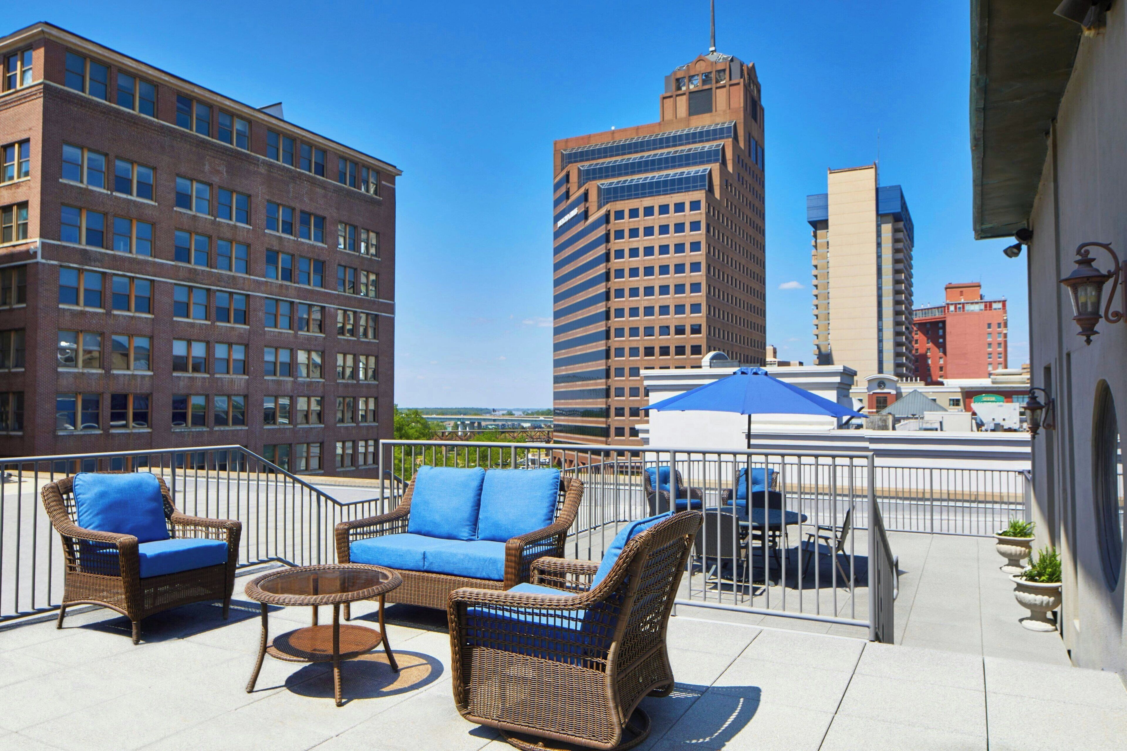 A rooftop terrace with wicker furniture, a round table, and a view of city buildings.
