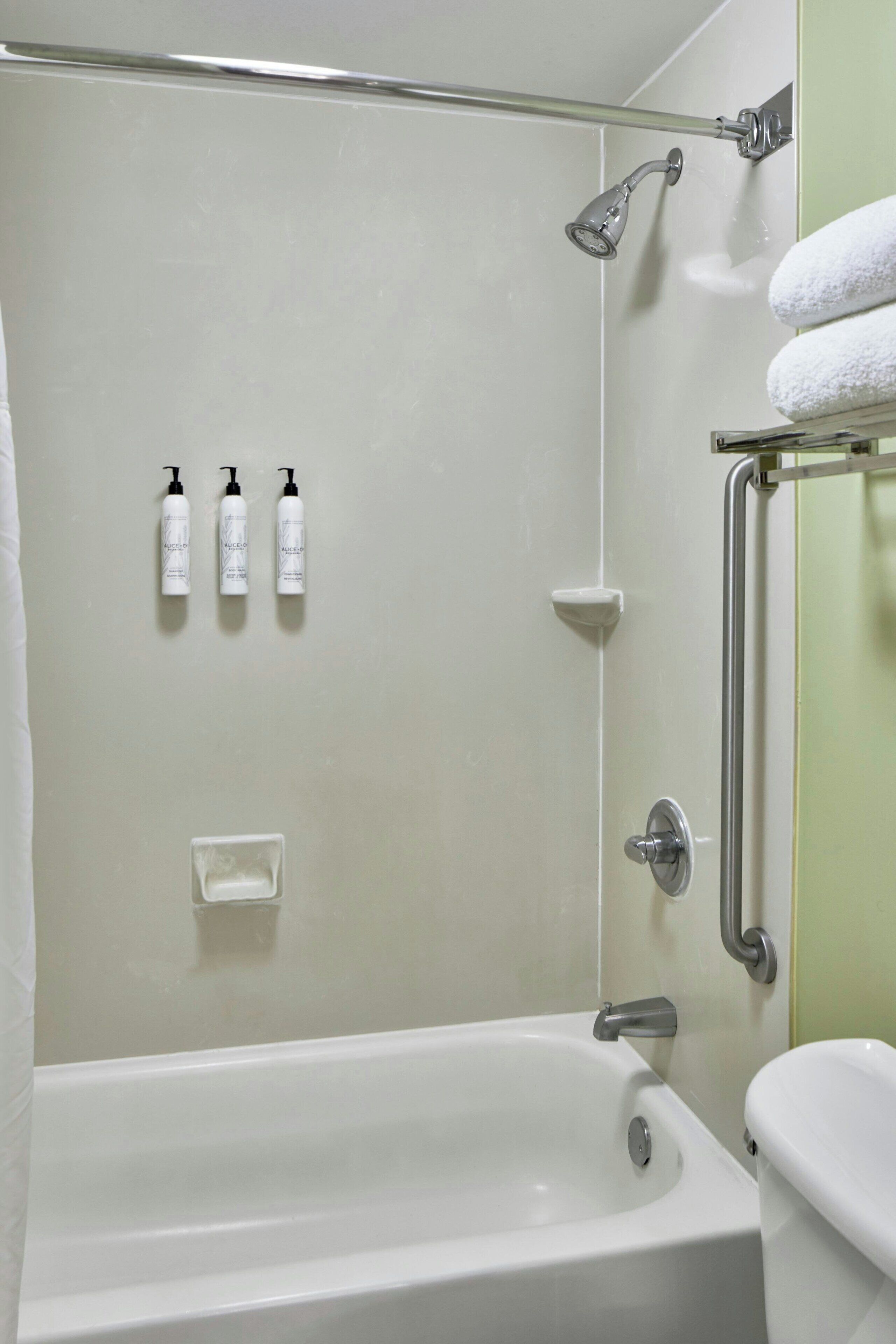 A bathroom with a bathtub, a toilet, a showerhead, and three bottles of shampoo on the wall.