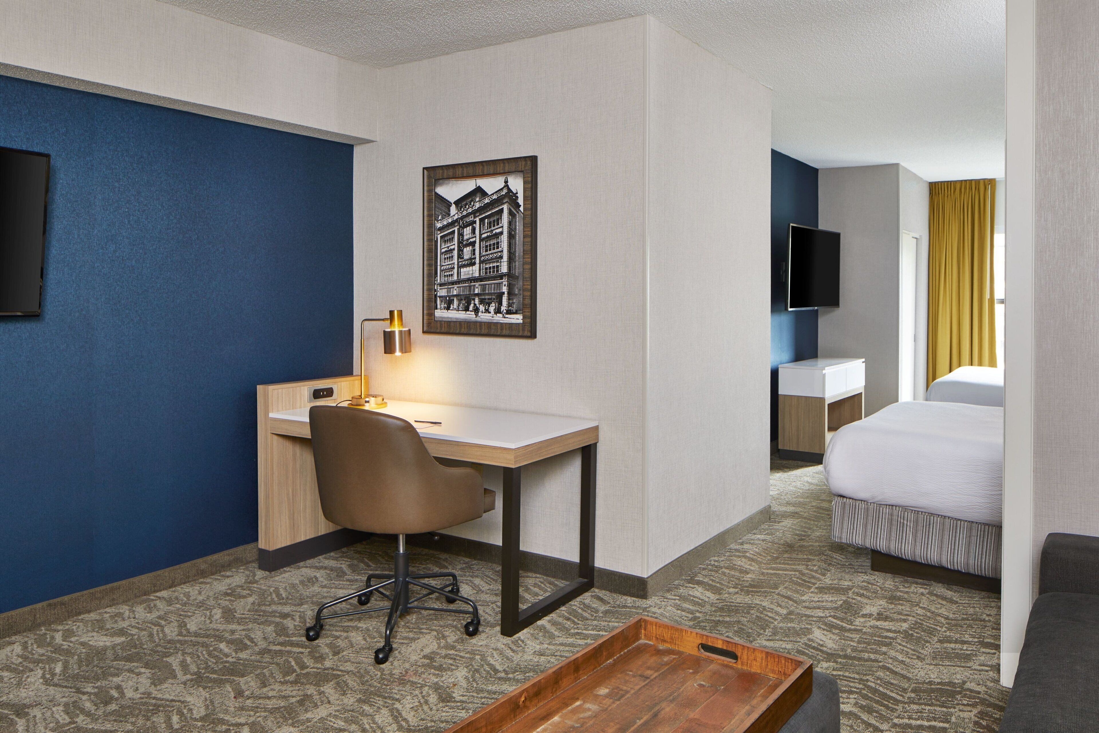 Une chambre d’hôtel équipée d’un bureau, d’une chaise, d’un lit et d’un téléviseur fixé au mur.