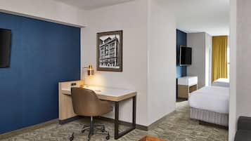 A hotel room with a desk, chair, bed, and a mounted TV.
