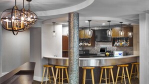 A modern bar area with a central column, bar stools, a counter with a digital screen, and hanging pendant lights. - Springhill Suites By Marriott Memphis Downtown (Memphis)