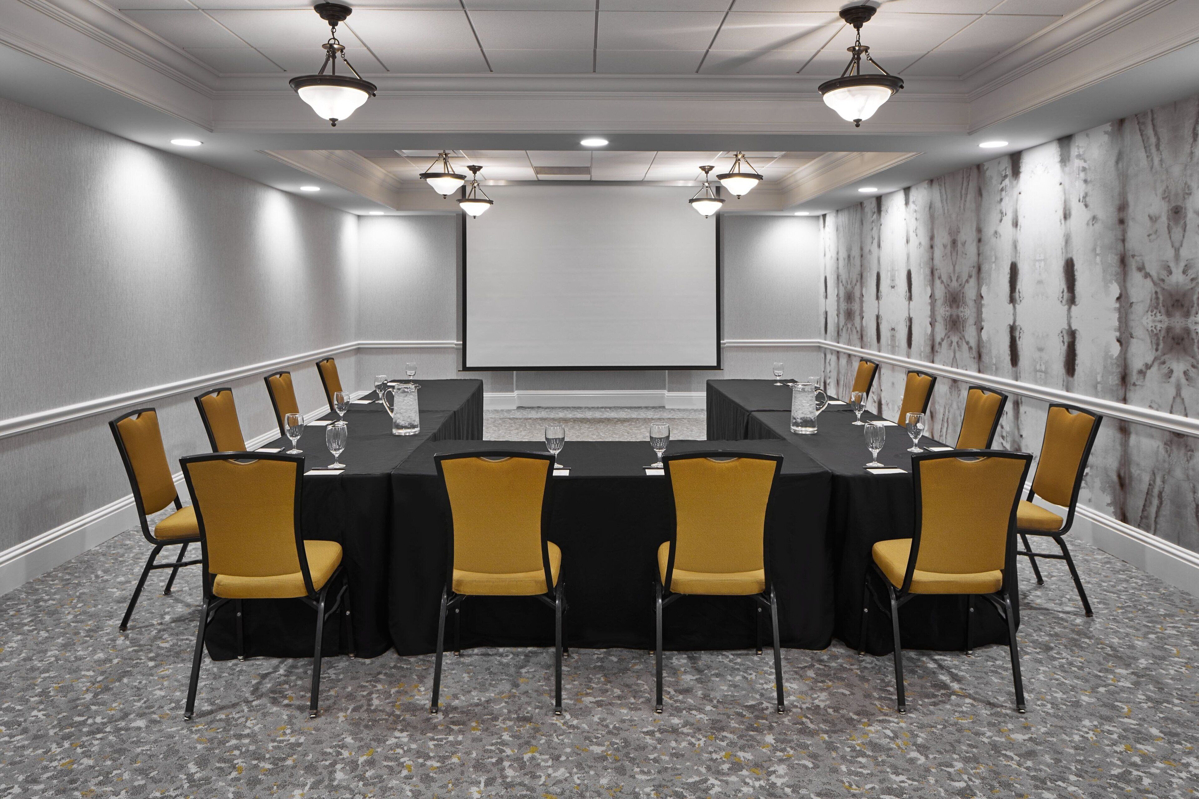 A conference room with a long table, yellow chairs, and a projector screen.