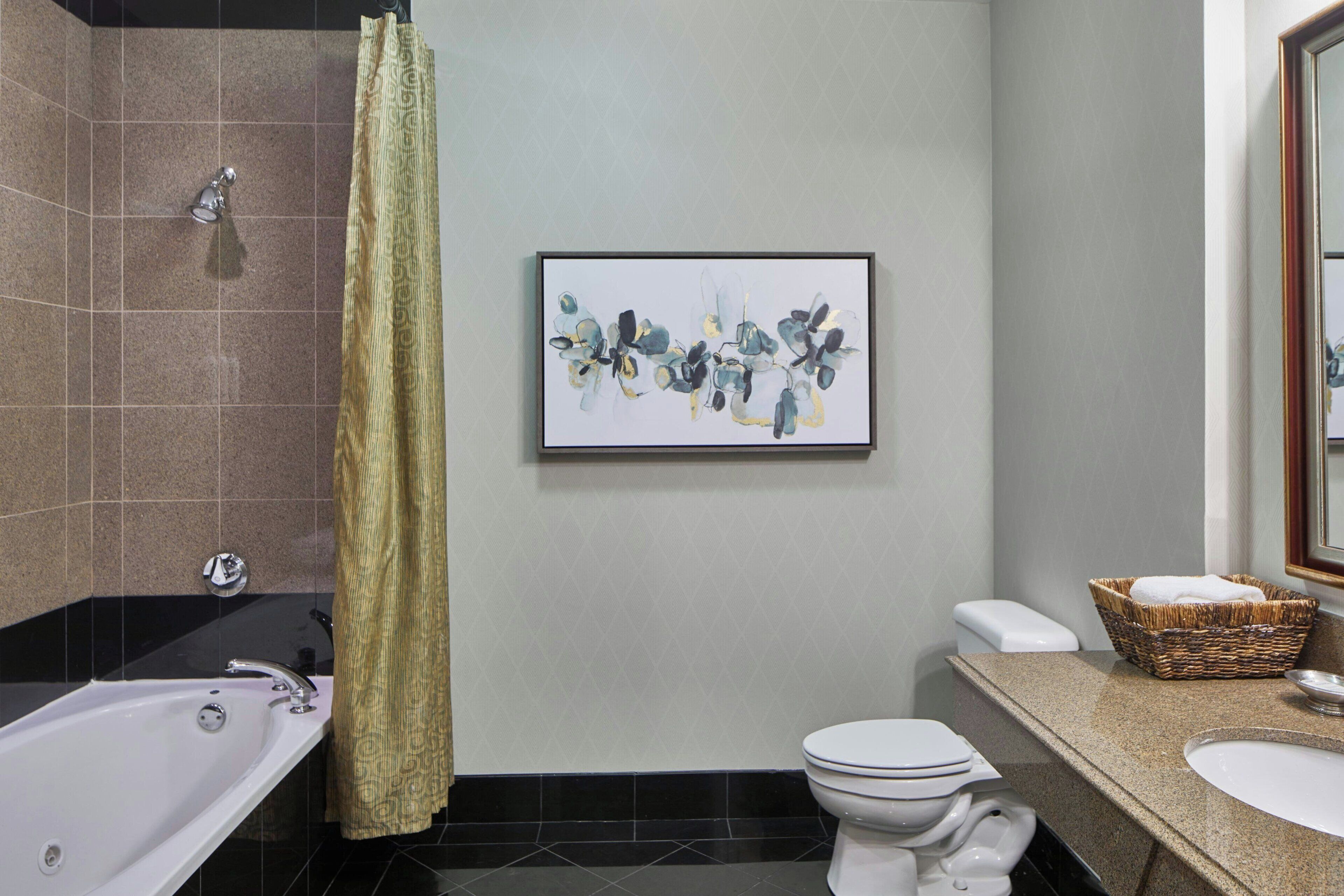 A bathroom with a bathtub, toilet, sink, and a framed abstract painting on the wall.