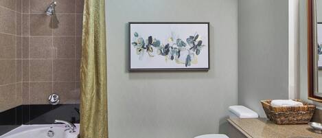 A bathroom with a bathtub, toilet, sink, and a framed abstract painting on the wall.