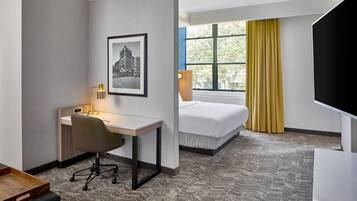 Habitación de hotel con escritorio, silla, cama y un ventanal con cortinas amarillas.
