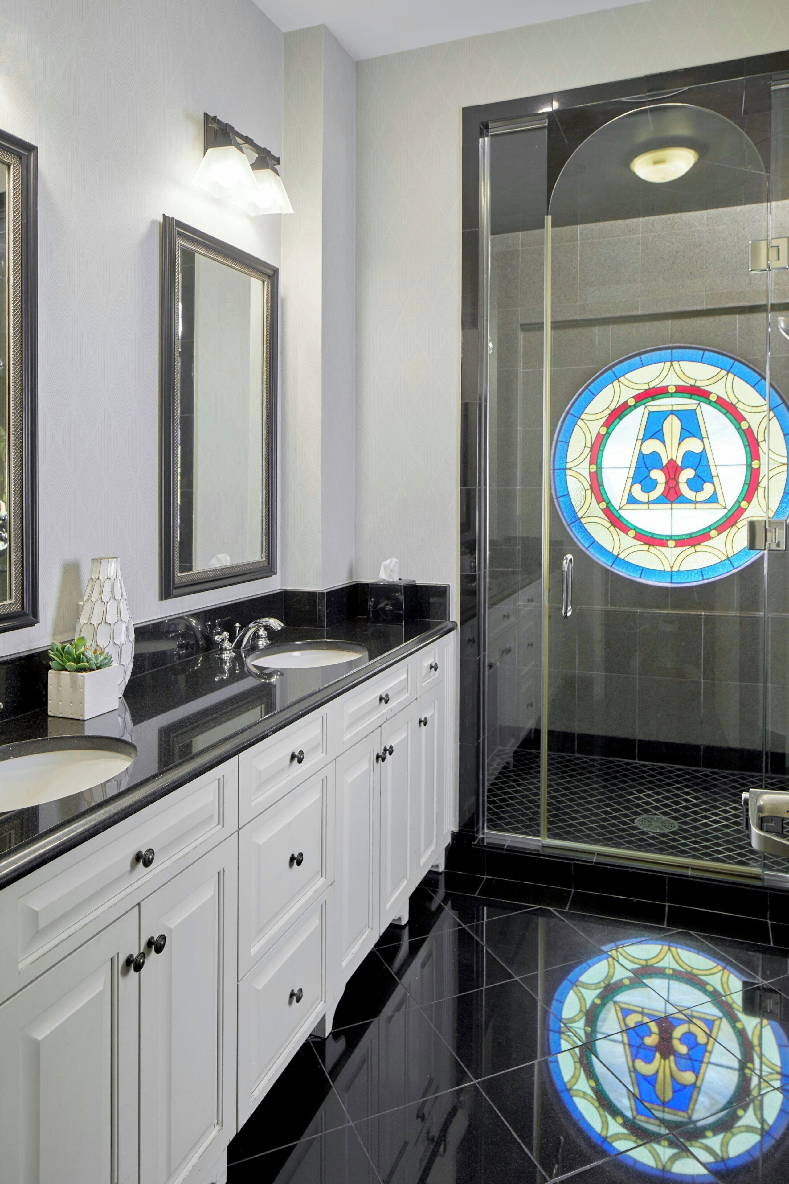 A modern bathroom with two sinks, a glass shower enclosure, and a decorative stained glass window.