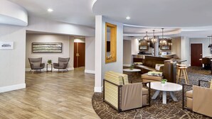 A modern hotel lobby with a curved ceiling, a reception desk, seating areas, and a kitchen visible in the background. - Springhill Suites By Marriott Memphis Downtown (Memphis)