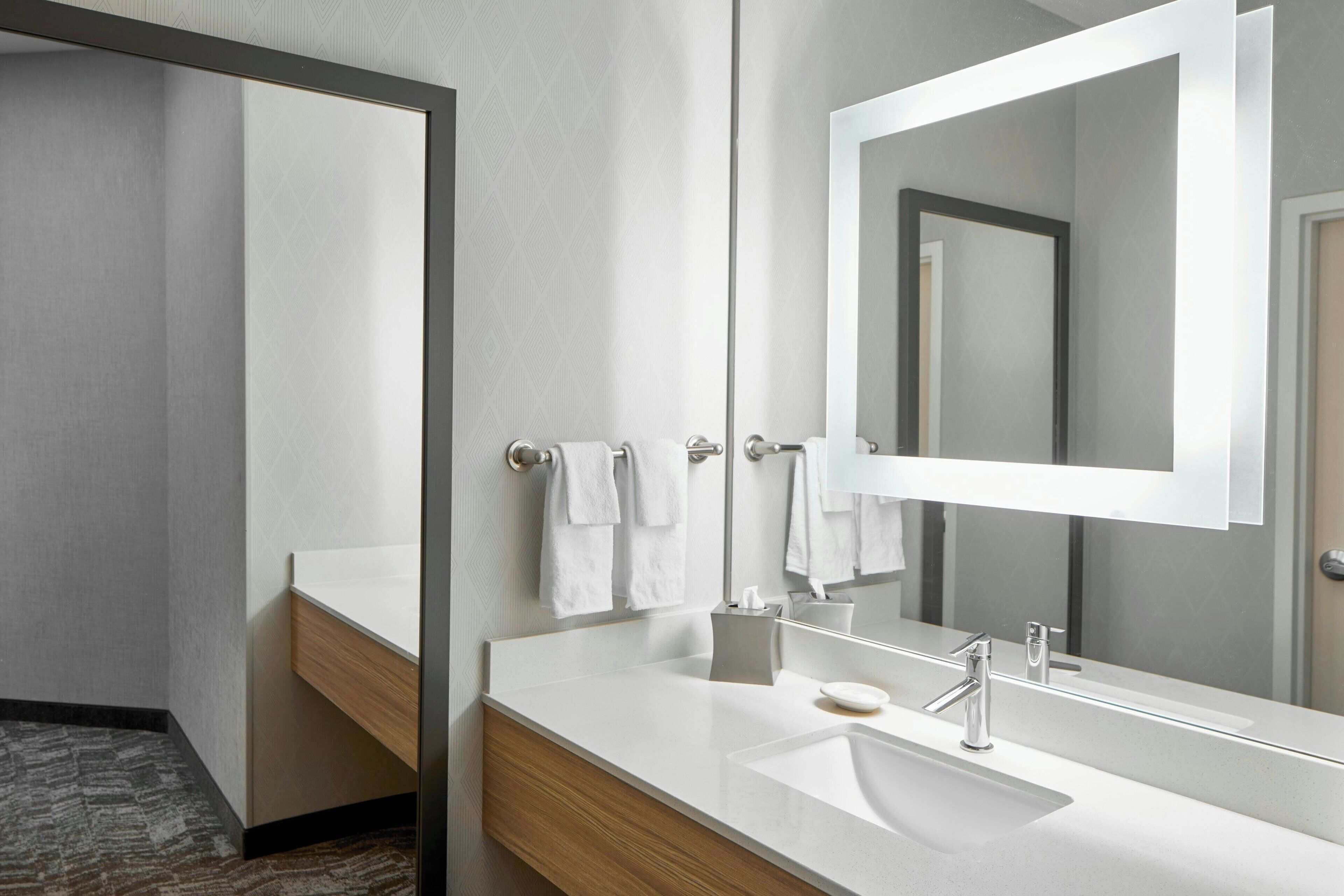 A modern bathroom with a large mirror, a white sink, and a wooden vanity.