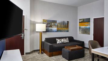 A hotel room with a sofa, a coffee table, a desk, a lamp, and artwork on the walls.