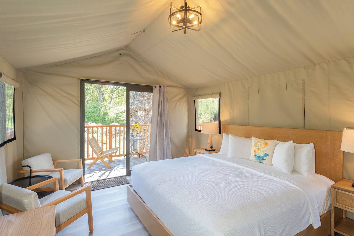Ein Zeltraum mit einem großen Bett, einem Sessel, einem Tisch und Blick ins Freie.